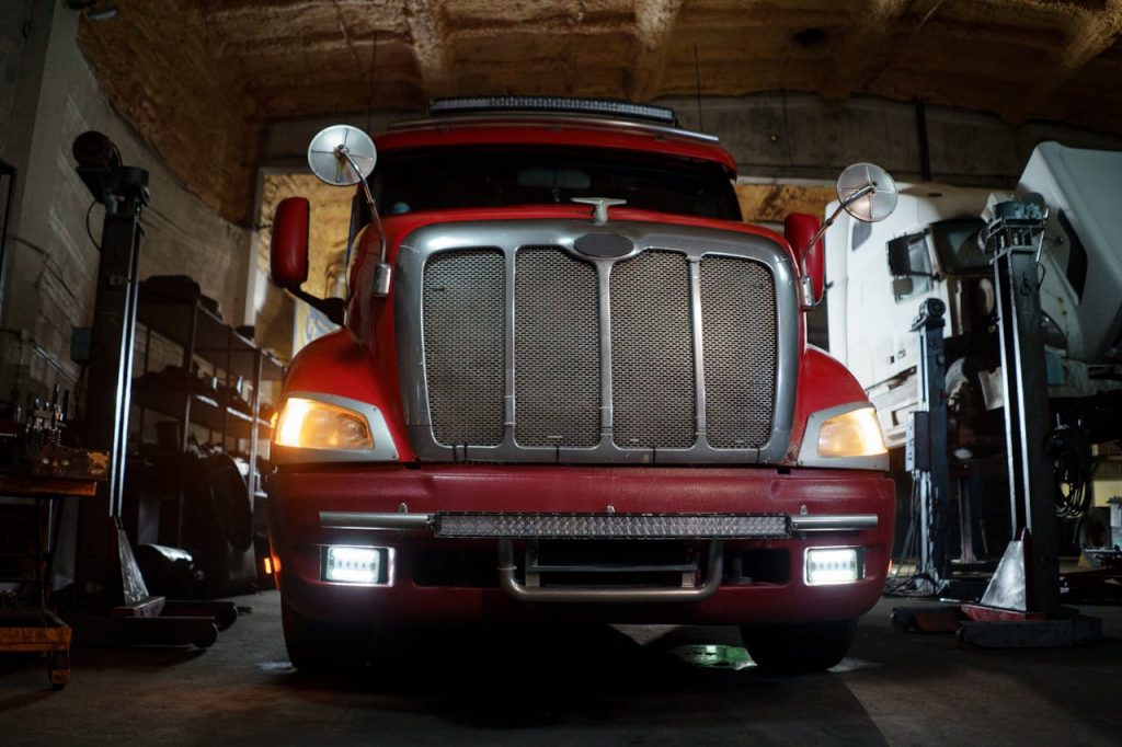 Front view of a red truck in a dimly lit automotive repair shop with a focus on the grill and headlights.